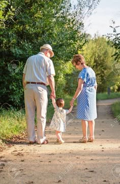 an older man and woman holding hands while walking with a small child on a path