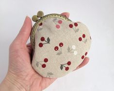 a hand holding a coin purse with cherries and leaves on the front, in white background