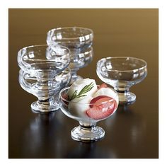 four clear glass bowls with fruit in them on a black table top, one bowl is filled with ice cream and the other two are empty