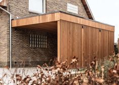 a brick building with wooden slats on the front and side walls, next to some bushes