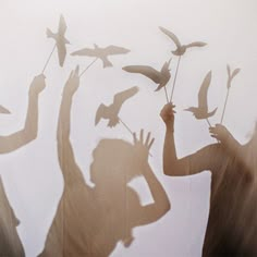 two people are casting shadows on the wall with birds in their hands and one is holding a stick