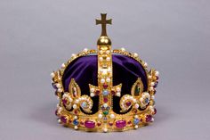 a purple crown with pearls and a cross on the top is sitting in front of a gray background