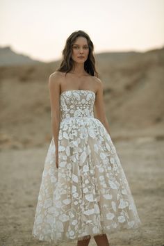 a woman standing in the desert wearing a strapless dress with flowers on it's waist