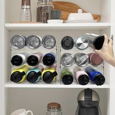 a person holding a coffee cup in front of a shelf filled with cups