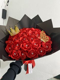 a bouquet of red roses with a gold crown on top is being held by someone's hand