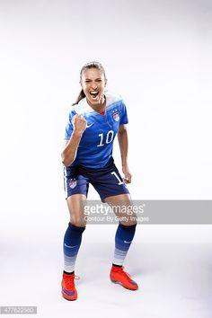 a female soccer player posing for the camera with her fist up and smiling at the camera