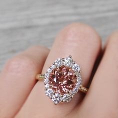 a close up of a person's hand holding a ring with a pink diamond