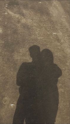 two people standing next to each other in the street with their shadows on the ground