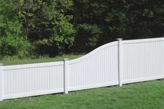 a white fence in the middle of a grassy area with trees and bushes behind it