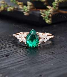 an emerald and diamond ring sitting on top of a wooden table next to some plants