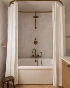 a white bath tub sitting next to a wooden stool under a shower faucet