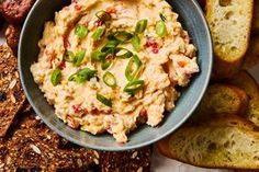 a bowl filled with hummus next to sliced bread and crackers on the side