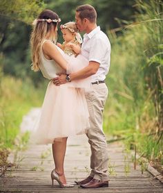 a man, woman and child standing on a wooden walkway in front of tall grass