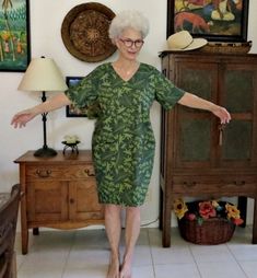 an older woman is standing in front of a dresser and chair with her arms outstretched