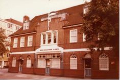 an old brick building with several windows and doors on the front, along with other buildings in the background