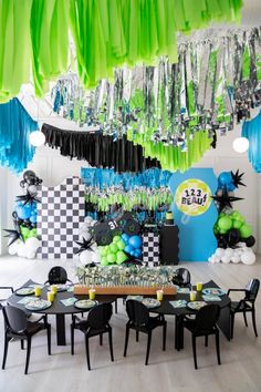 a room filled with lots of green and blue balloons hanging from the ceiling next to black chairs