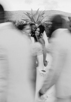 black and white photo of bride and groom with pineapple on their head, surrounded by blurry people