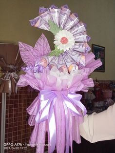 a woman is holding a bouquet made out of dollar bills and purple ribbon with flowers on it