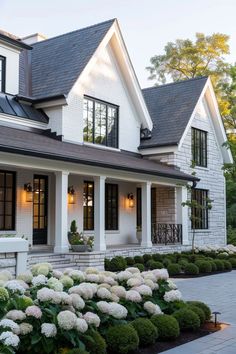 a white house with lots of windows and flowers in the front yard, surrounded by greenery