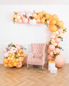 an arch made out of balloons and oranges is displayed in front of a pink chair