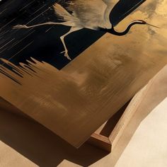 a large bird flying over a wooden table with black and gold paint on it's surface