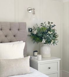 a bedroom with a white bed and flowers in a vase on the nightstand next to it