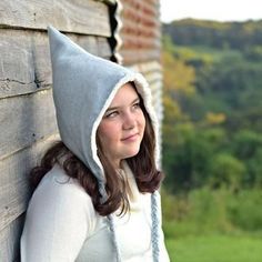 a woman with a hood on her head leaning against a wooden wall and looking off into the distance