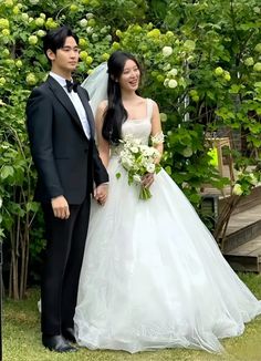 a man and woman standing next to each other in front of some bushes with flowers