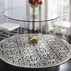 a round glass table with clear chairs and a rug on the floor in front of it