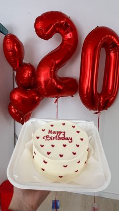 a birthday cake on a plate with balloons in the shape of number twenty and heart shapes