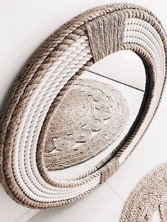 an oval mirror with rope around it on the wall next to another round mirror and rug