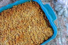 a casserole dish with crumbled toppings sits on a table next to flowers