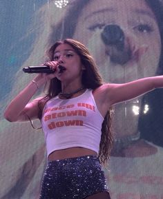 a woman in a white tank top and silver sequin skirt holding a microphone up to her mouth