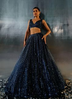 This stunning Blue Sequins Embroidered Bridal Lehenga Set is the epitome of elegance and modernity. Crafted from soft net fabric, the blue lehenga is adorned with intricate abstract motifs, dazzling with tonal sequins, crystals, and bugle beads that catch the light beautifully. The floor-length skirt flows gracefully with every step, exuding a timeless charm. Teamed with a luxurious blouse featuring a flattering plunging neckline and voluminous design, this ensemble is completed with a matching dupatta, elegantly embellished along the border. Perfect for the bride or bride-to-be for a Cocktail or Reception, this lehenga set promises to make you stand out with its exquisite craftsmanship and contemporary allure. Composition : Lehenga, Blouse and Dupatta - Net Care: Dry Clean Only and Vacuum Embroidered Bridal Lehenga, Abstract Motifs, Blue Lehenga, Lehenga Blouse, Floor Length Skirt, Net Fabric, Bugle Beads, Bridal Lehenga, Plunging Neckline