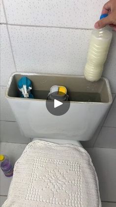 a person is using a bottle to fill up a container on the back of a toilet