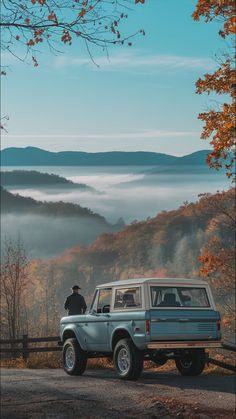 a man standing on top of a car next to a forest filled with trees and fog