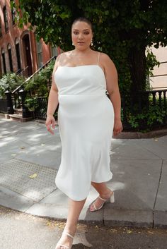 a woman in a white dress is walking down the street with her hand on her hip