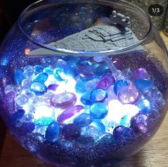 a fish bowl filled with lots of blue and purple rocks on top of a wooden table