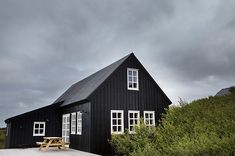 a black house sitting on top of a lush green hillside next to a wooden bench