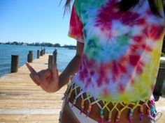 a woman is standing on a dock with her hand in her pocket and wearing a tie dye shirt