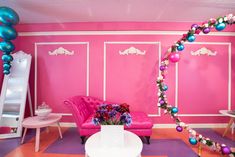 a living room decorated in pink and purple with balloons on the wall, couches and tables