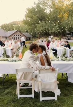 a bride and groom sitting at a table in the middle of an outdoor wedding reception