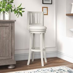 a white bar stool next to a wooden cabinet and potted plant in a room