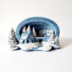 a small blue plate with a house and trees on the front is sitting on a white surface