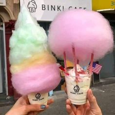 two ice cream sundaes are being held up in front of each other with pink, green and yellow fluffy balls on top