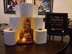 a stack of toilet paper sitting on top of a wooden table next to a sign that says the tree is amazing do you like my igloo?