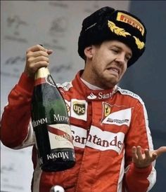 a man in a red and white suit holding a bottle of champagne while standing next to a microphone