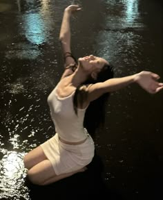 a woman in white shirt and shorts standing in water with her arms raised above her head