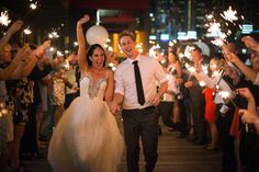 a bride and groom walking through a crowd holding sparklers