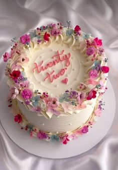 a white cake with pink and blue flowers on it that says happy birthday to you